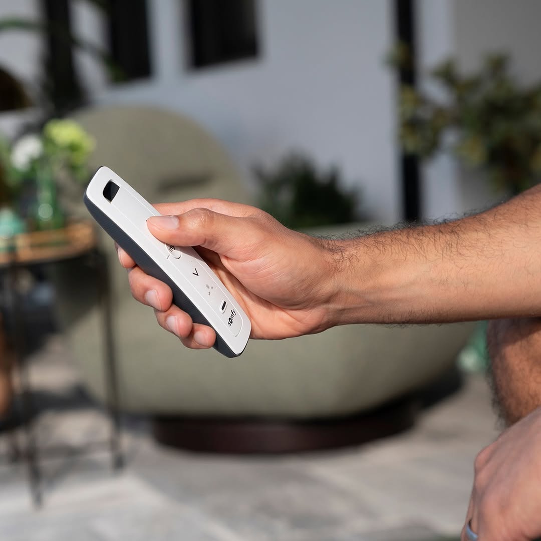 Person using a Somfy handheld remote on a sunlit terrace