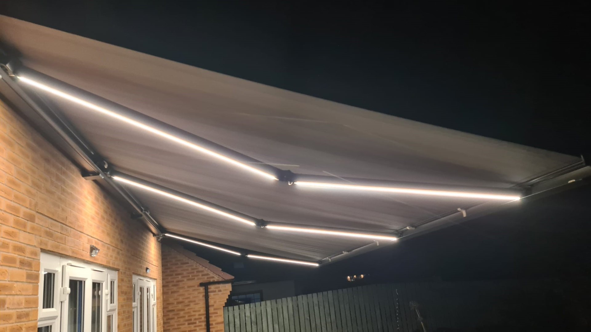 Wide awning with dual LED strips lighting up a rear garden at night