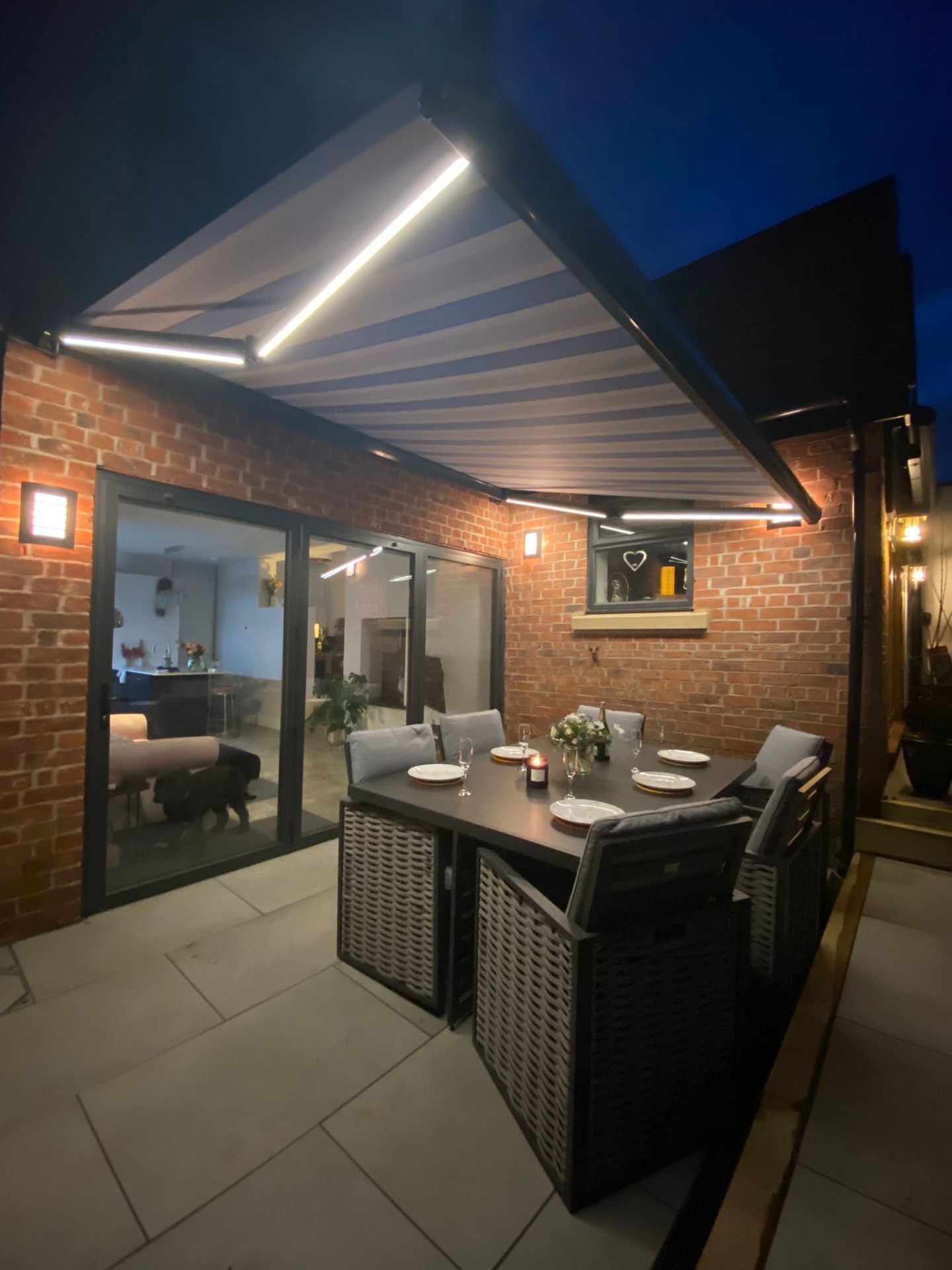 Aura awning with integrated LED arm lighting over a lit brick-walled terrace at night